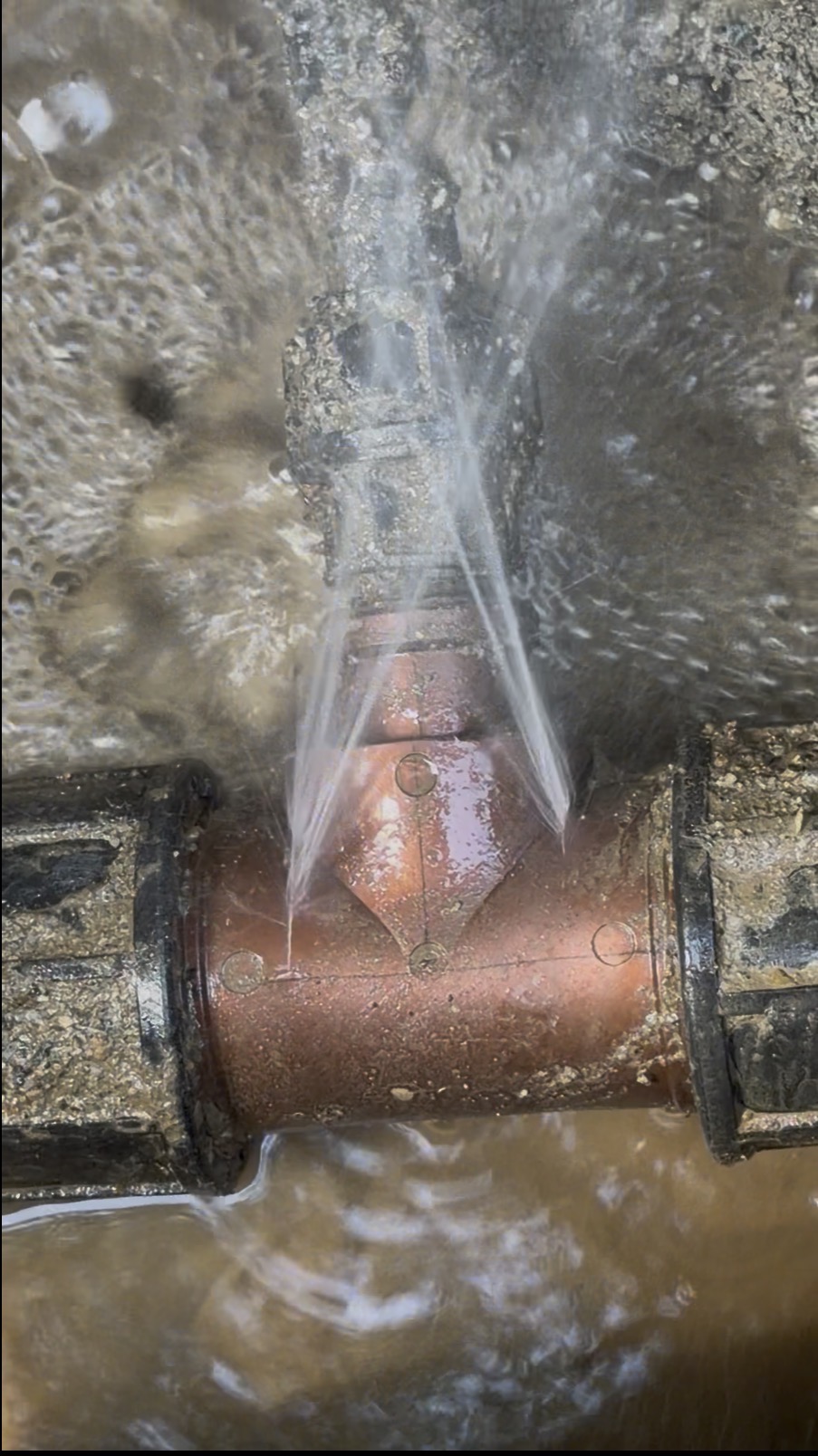 Water main leak spraying from a damaged fitting under a West Vancouver driveway before repair